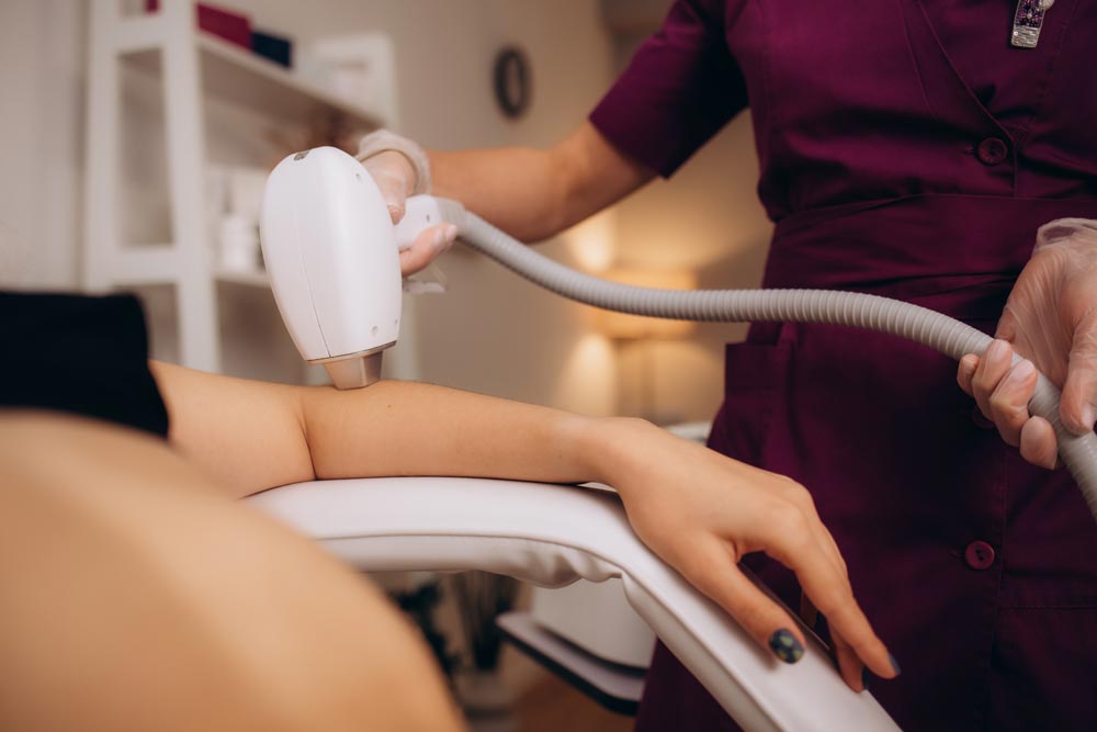 Spa technician performing laser skin treatment on client using professional aesthetic laser device